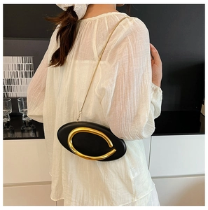 Detail of black oval crossbody bag with large gold horseshoe metal handle and chain strap