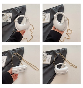 Detail view of white crescent bag with gold chain and circular handle on artistic background