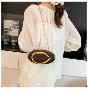 Deep brown oval bag with golden metal hardware and chain strap shown on a model's shoulder