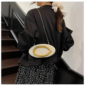 Detail of white oval crossbody bag with large gold buckle and slim metal chain strap