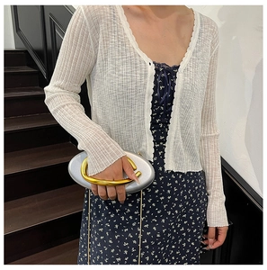 Detail of elegant silver oval handbag with gold ring handle and white ribbed cardigan