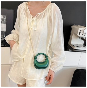 Detail view of a dark green crescent bag with a gold chain on a white linen outfit