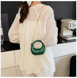 Detail of green crescent acrylic handbag featuring round metal handle and gold chain strap