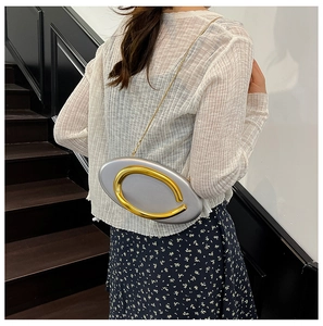 Silver metallic oval clutch bag with gold C-buckle and chain strap shown on a model