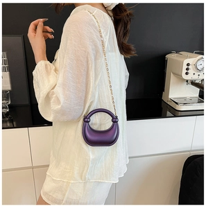 Chic purple crescent evening bag with gold chain strap shown in a modern interior setting