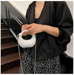 White crescent evening bag with gold chain strap shown on a model in a minimal setting