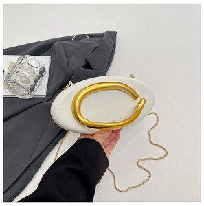 Close-up of white oval fashion handbag with large gold metal handle and chain