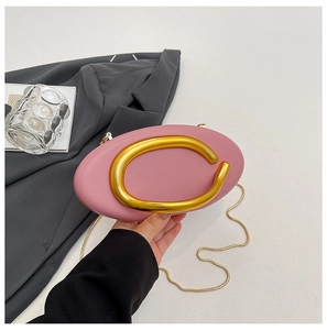 Detail of pink oval clutch bag featuring a gold C-shaped metal handle and snake chain