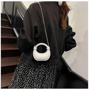 Detail of white acrylic crescent bag with circular handle and gold chain on model