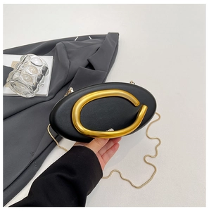 Detail of black oval evening bag with large gold horseshoe handle and fine snake chain