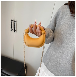 Detail of a crescent yellow mini bag with gold chain strap on a model's arm