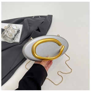 Detail of silver oval clutch bag featuring a bold gold C-shaped buckle and chain strap