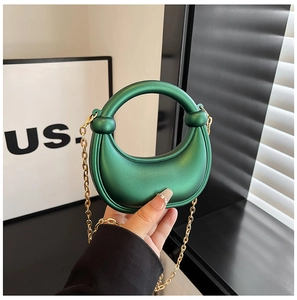 Detail of emerald green crescent bag with round handle and gold metal chain strap