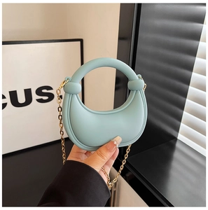 Detail of mint green crescent bag with circular handle and gold chain strap