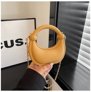 Detail of a bright yellow crescent acrylic handbag with a round handle and gold metal chain