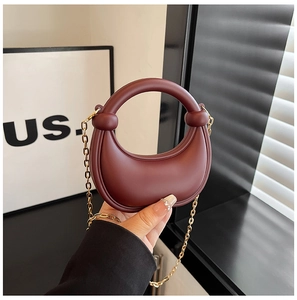 Detail of burgundy crescent moon mini bag featuring gold chain and thick round handle