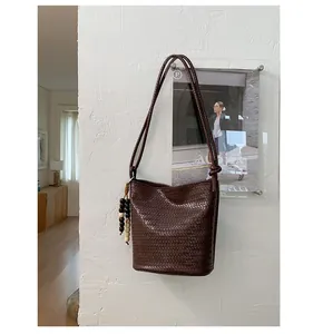 Detail of dark brown woven bucket bag with vintage beads tassel on white textured wall