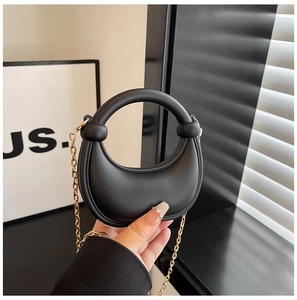 Detail of minimalist black matte crescent bag with gold chain and round top handle
