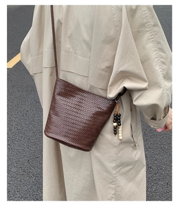 Detailed texture of dark brown woven bucket bag with stylish beaded tassel on beige trench coat