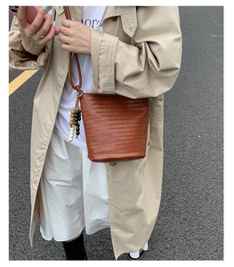 Brown woven bucket bag with retro wooden beads detail shown on a street model