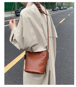 Detail of a brown woven leather bucket bag featuring a beaded charm and slim shoulder strap