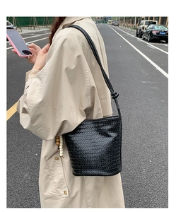 Detail of black woven bucket bag with beaded charm accessory on a street background