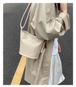 Close-up of cream woven bucket bag featuring detailed bead charms and thin rope straps