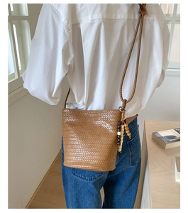 Detail of a brown woven bucket bag with unique wooden bead tassels and PU leather texture