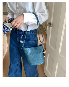 Detail view of a blue woven bucket bag featuring vintage wooden bead charm and long straps