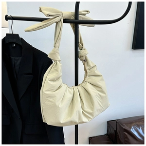 Close-up of beige shoulder bag featuring pleated texture and a large decorative bow