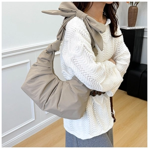 Detail of beige pleated hobo bag with a large bow on shoulder strap worn by a model