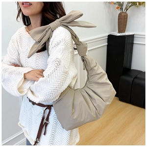 Detail view of beige pleated shoulder bag with large bow decoration on strap