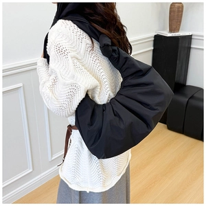 Detail of black crescent shoulder bag featuring pleated texture and decorative knot strap