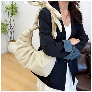 Detail of cream pleated cloud bag featuring large bow shoulder strap and soft faux leather texture