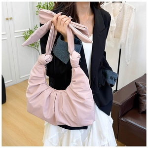 Detailed view of pink pleated shoulder bag featuring a large bow and silky fabric texture