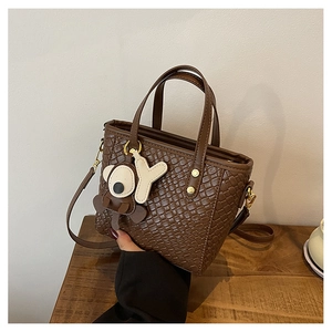 Détail d'un sac seau marron foncé à texture tressée avec bijou de sac koala et doré