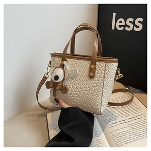 Détail d'un sac seau tissé blanc cassé avec poignées en cuir marron et charme de chien