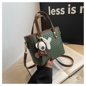 Détail du sac seau tissé vert foncé avec poignées en cuir marron et pendentif singe