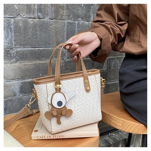 Détail du sac seau tissé blanc avec poignées en cuir marron et pendentif animalier
