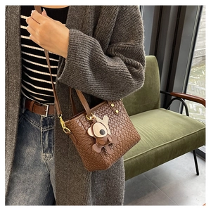 Gros plan du sac seau tissé marron avec charm ours et finitions en métal doré