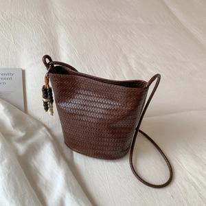 Deep brown woven bucket tote bag with beaded tassel on a soft white fabric background