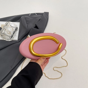 Pink oval leather handbag with large gold C-handle and chain, held by a model