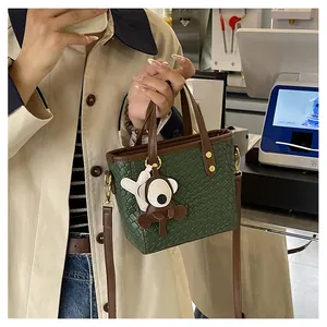 Détail du sac fourre-tout tissé vert forêt avec poignées marron et breloque singe en peluche