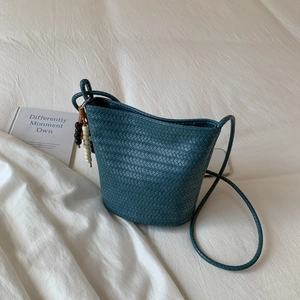 Minimalist woven bucket tote bag with beaded charm on white fabric background