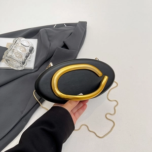 Elegant black oval evening bag with large gold C-shaped handle and slim metal chain