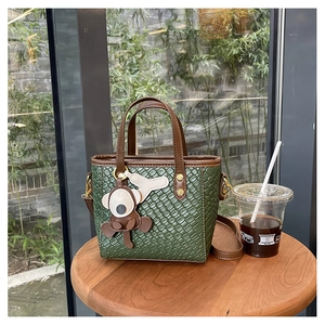 Détail du sac seau tissé vert olive avec anses marron et breloque en forme de singe