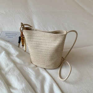 Minimalist cream woven bucket tote bag with wooden bead charm on a soft fabric background