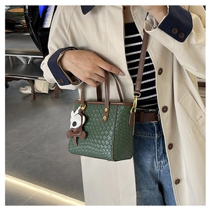 Détail du sac seau en cuir tressé vert avec bandoulière marron et breloque singe