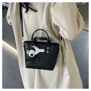 Détail du sac seau noir tressé avec garnitures dorées et pendentif ours sur modèle