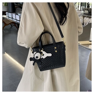 Détail du sac seau noir tressé avec clous dorés et pendentif décoratif en forme d'ours